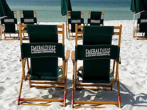 Beach chairs with 'Emerald Isle Gulf Front Condominiums' branding, arranged on a sandy beach with ocean in the background.