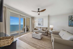 Un salon spacieux avec un balcon, un ventilateur de plafond, un canapé, une table basse et une lampe.