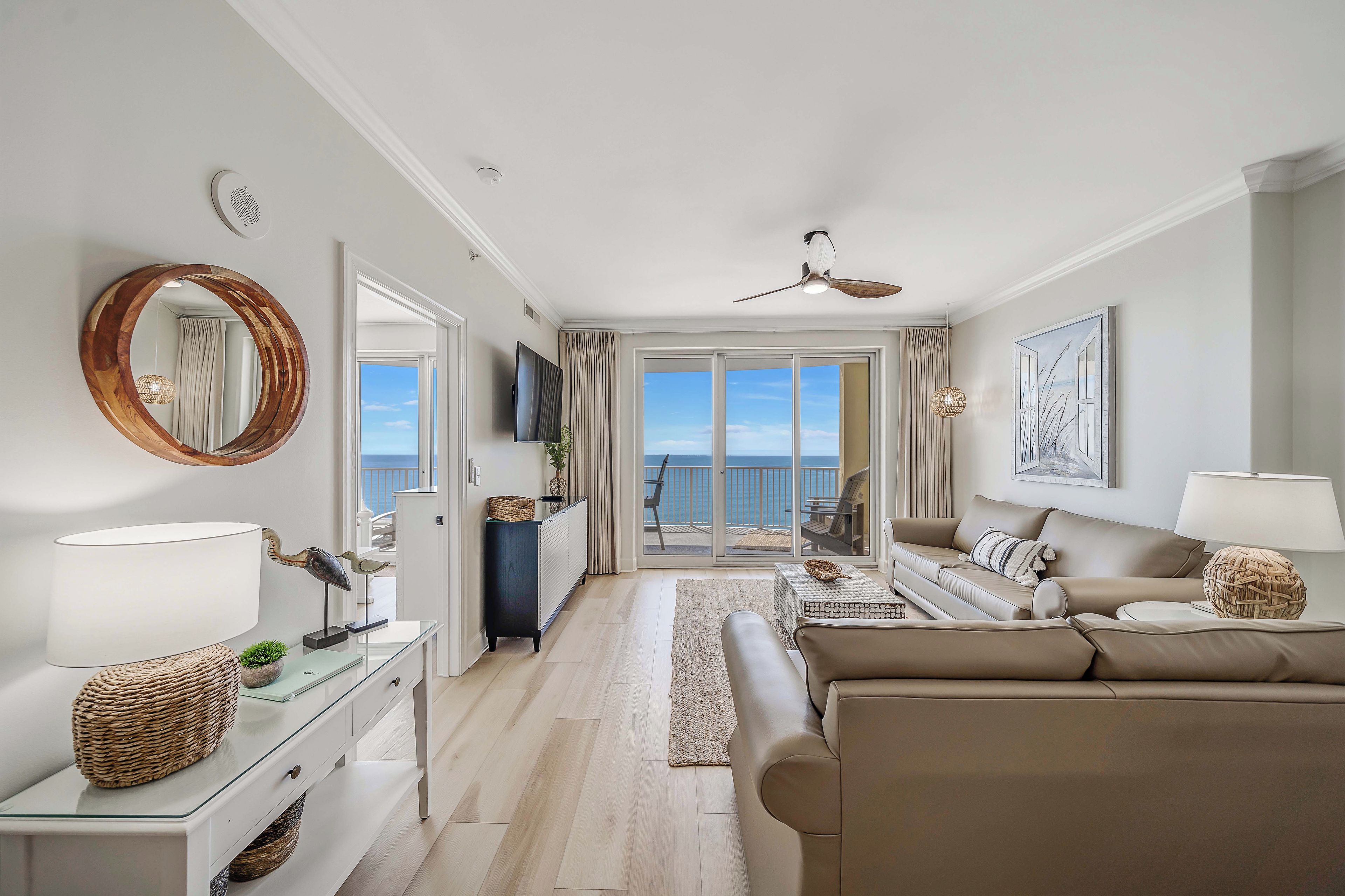 Een moderne woonkamer met een bank, een salontafel en een televisie. Er is een balkon met uitzicht op zee.