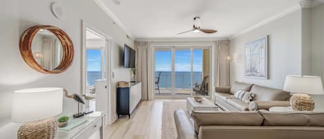 Een moderne woonkamer met een bank, een salontafel en een televisie. Er is een balkon met uitzicht op zee.