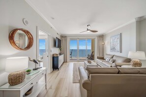 Een moderne woonkamer met een bank, een salontafel en een televisie. Er is een balkon met uitzicht op zee.