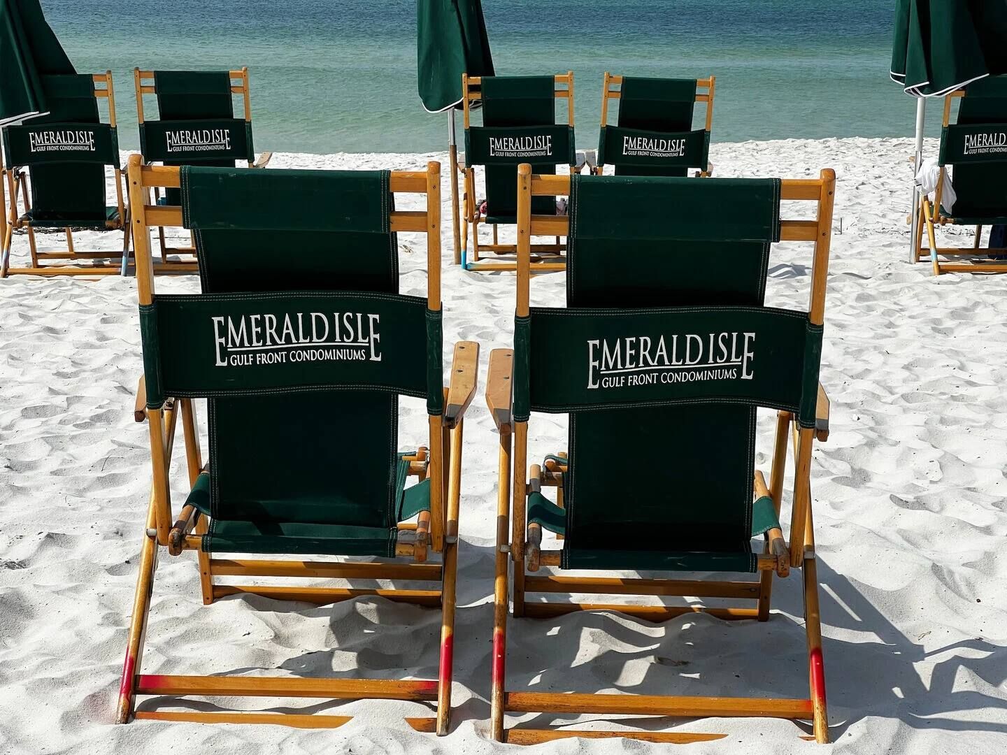 Des chaises de plage portant la marque « Emerald Isle Gulf Front Condominiums », disposées sur une plage de sable avec l’océan en arrière-plan.