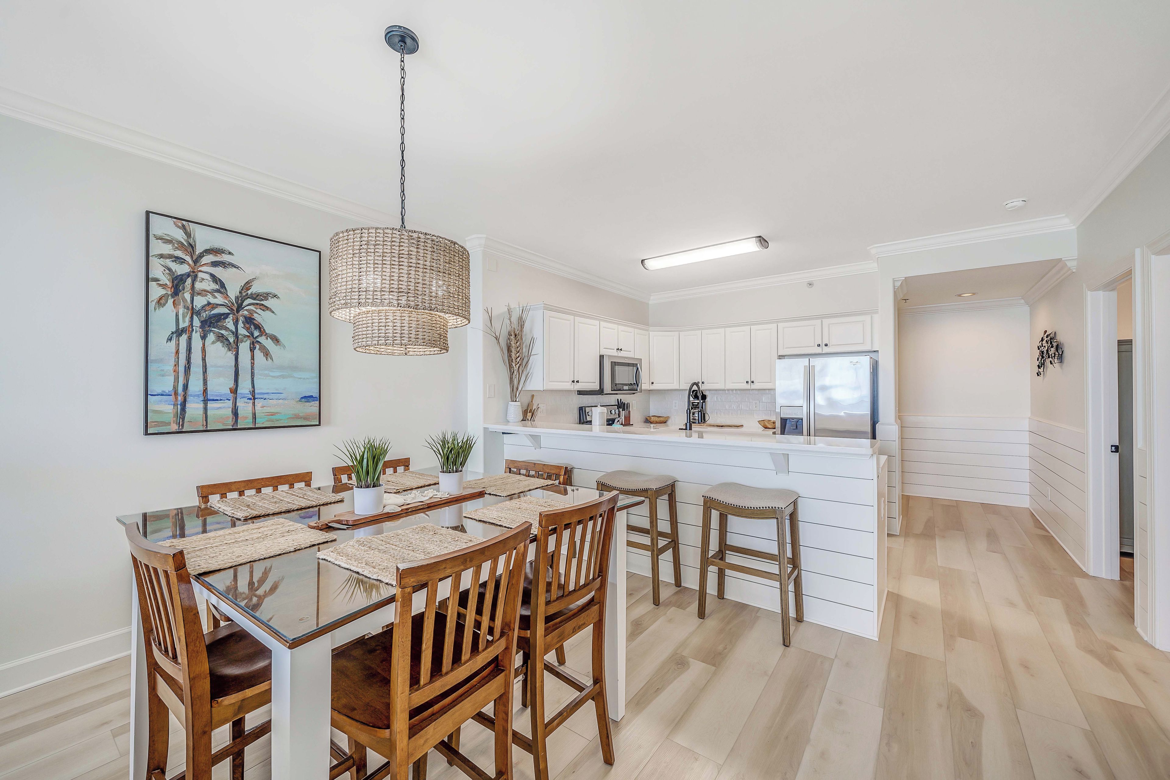 A modern kitchen with white cabinets, a central island, and a dining area with wooden chairs and a glass table.