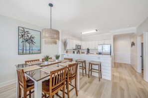 A modern kitchen with white cabinets, a central island, and a dining area with wooden chairs and a glass table.