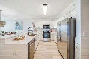 Een moderne keuken met witte kasten, roestvrijstalen apparatuur en een licht houten vloer.