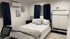 Un dormitorio ordenado con cama, escritorio y un equipo de aire acondicionado en la pared.