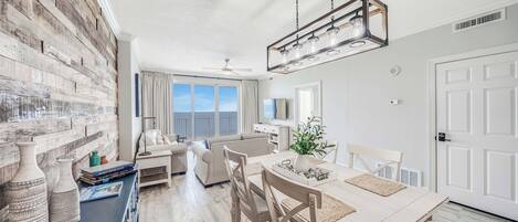 Een moderne woonkamer met een groot raam, een eethoek met een houten tafel en een inbouw wand van baksteen.