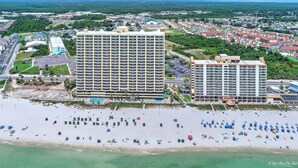 A large hotel with multiple floors, a pool, and a beach area with numerous umbrellas. - NEW Emerald Isle 2107 "Manta Ray Villa" Pool, FREE Perks&Beach Service for 4! (Panama City Beach)