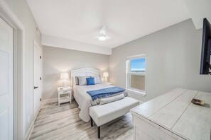 A bedroom with a bed, bedside tables, a bench, a ceiling fan, and a window with a view.