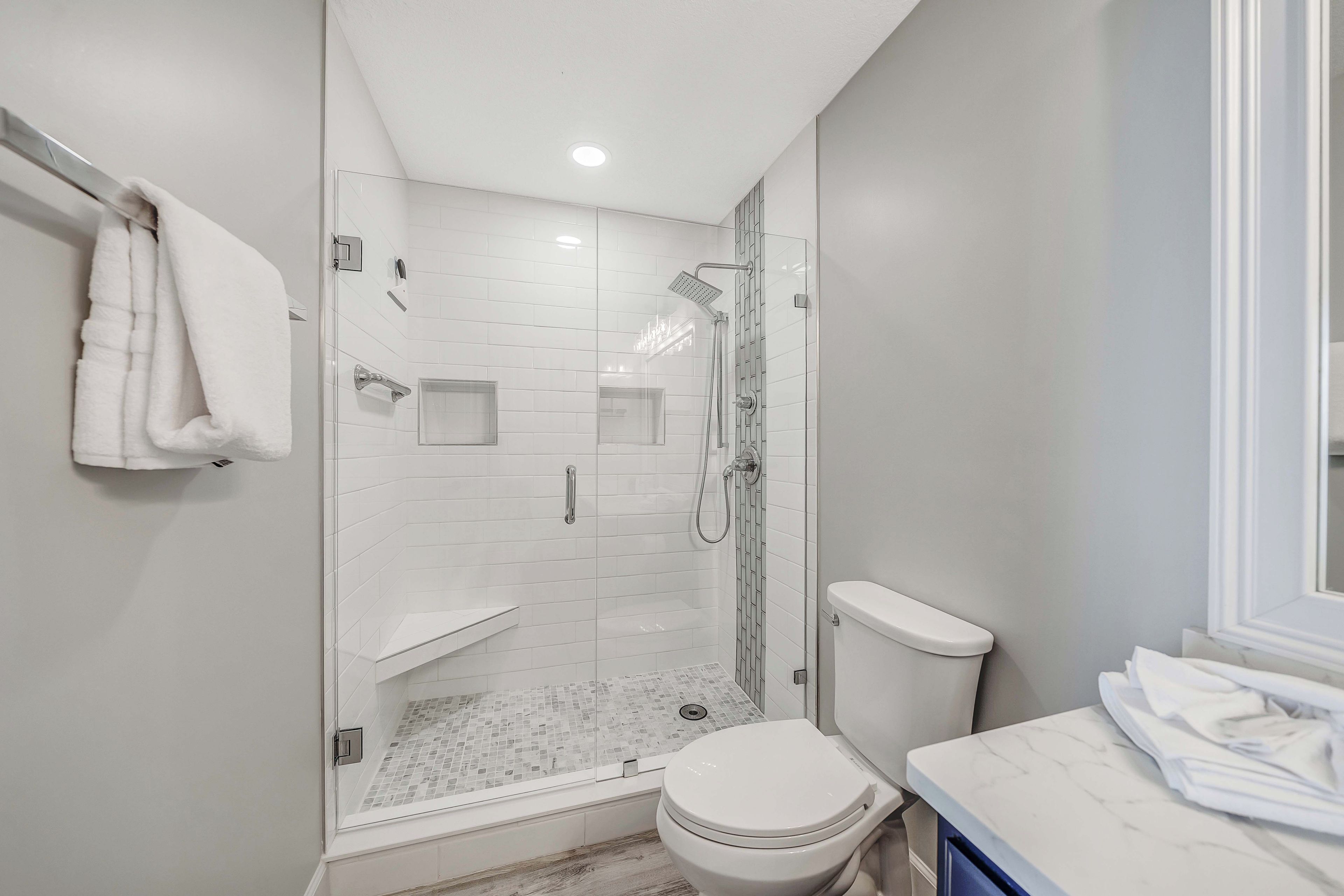 Een moderne badkamer met een douchecabine van glas, een toilet en een marmeren aanrechtblad.