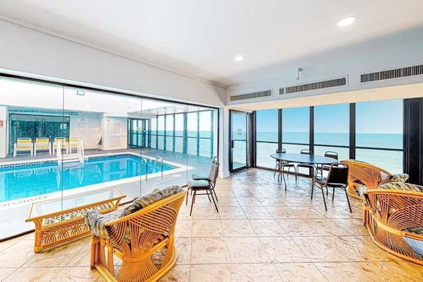 A spacious indoor area with a pool, wicker furniture, and large windows offering ocean views.
