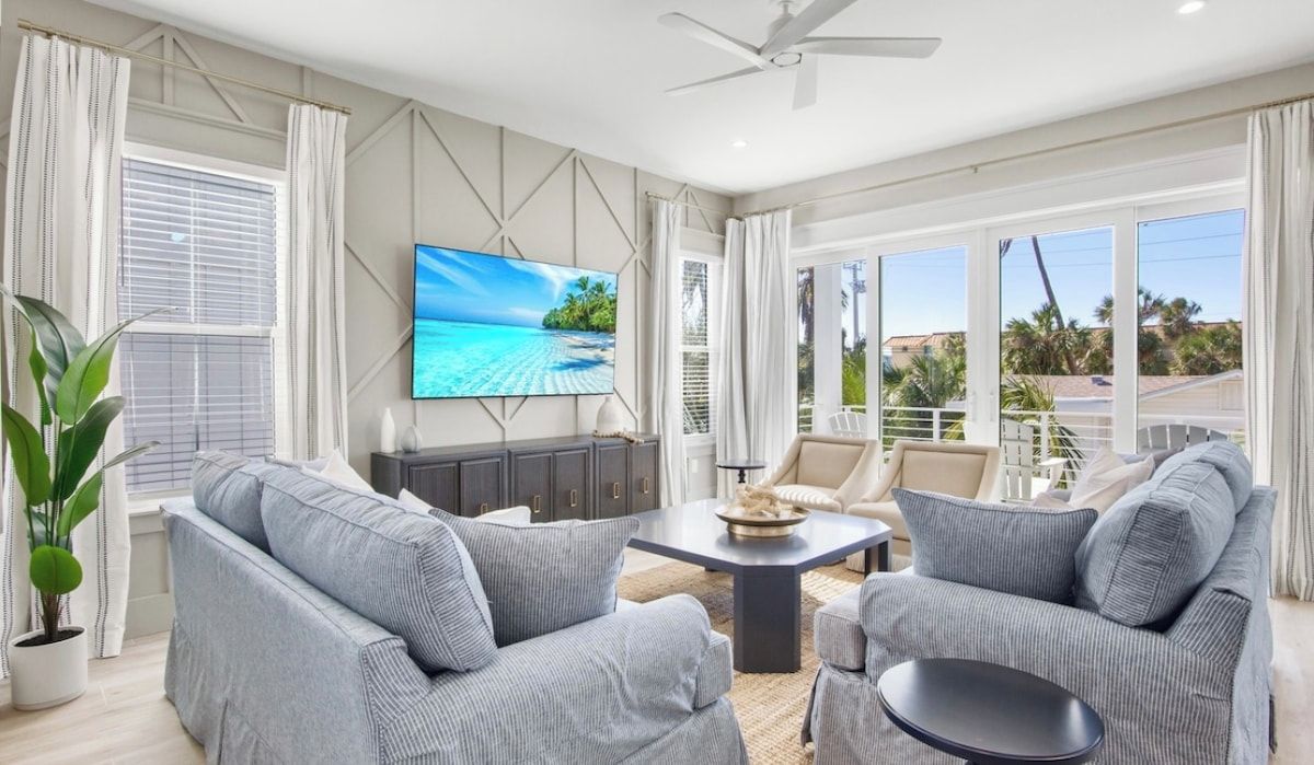 A modern living room with a flat-screen TV, grey sofas, a coffee table, and a ceiling fan.