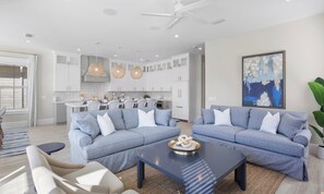 A modern living room with two sofas, a coffee table, and a dining area with a kitchen in the background.