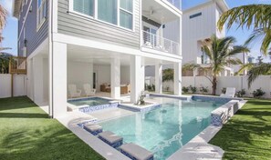 Ein zweistöckiges Haus mit Swimmingpool, Sitzgelegenheiten im Freien und einer überdachten Terrasse.