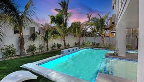 A swimming pool with a tiled edge, surrounded by palm trees and a white fence.