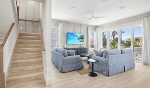 Ein großzügiges Wohnzimmer mit einem großen Fernseher, zwei grauen Sofas, einem Couchtisch und einer Treppe, die in einen oberen Bereich führt.
