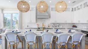 A modern kitchen with white cabinetry, a central island with seating, and three large wicker pendant lights.