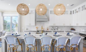 A modern kitchen with white cabinetry, a central island with seating, and three large wicker pendant lights.