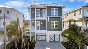 A two-story residential building with a balcony, a garage, and a well-maintained garden with palm trees.