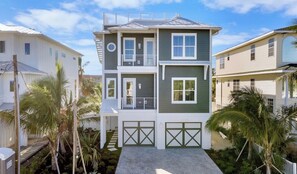 A two-story residential building with a balcony, a garage, and a well-maintained garden with palm trees.