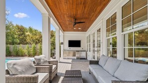 A covered outdoor patio with wicker furniture, a ceiling fan, and a TV mounted on the wall.