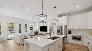 A modern kitchen with white cabinetry, a central island with a sink, and a dining area with a white sofa and chairs.