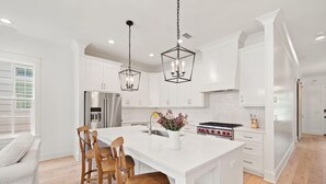 A modern kitchen with white cabinetry, a large island, stainless steel appliances, and pendant lighting.