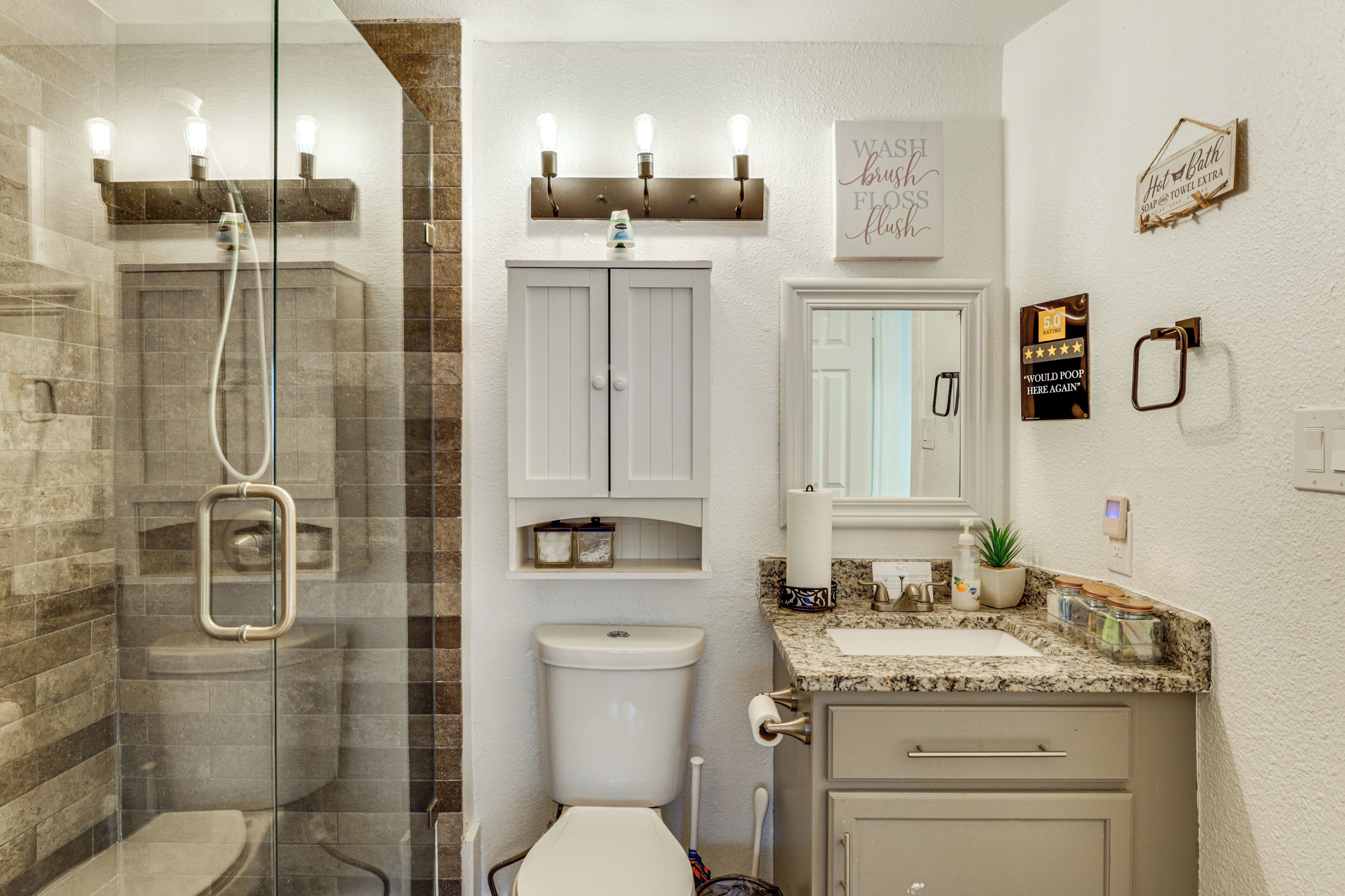 A bathroom with a glass-enclosed shower, a toilet, a sink with a marble countertop, and a vanity with drawers.