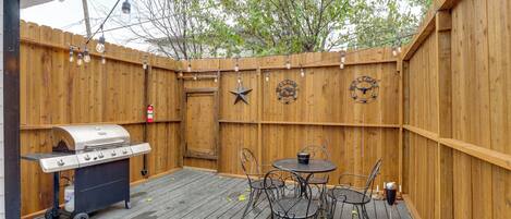Una terraza de madera con una parrilla de barbacoa, una mesa redonda con sillas y un reloj en la pared.
