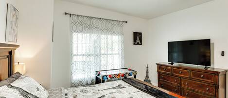 A bedroom with a bed, a dresser, a TV, a ceiling fan, and a window with patterned curtains.
