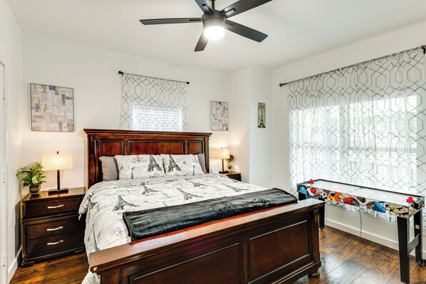 Une chambre à coucher avec un lit en bois, un ventilateur de plafond, une table de chevet avec une lampe et une fenêtre ornée de rideaux à motifs.
