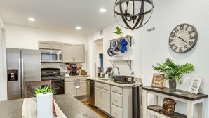 A modern kitchen with stainless steel appliances, a central island, and a chandelier.