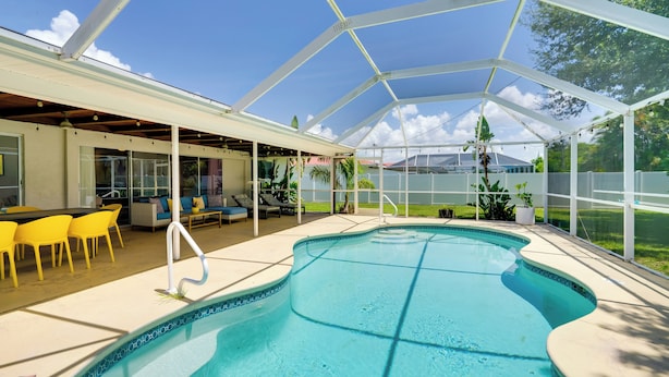 A covered outdoor swimming pool with a patio area, yellow chairs, and a table. - Heated Saltwater Pool < 2 Mi to Yacht Club Beach! (Cape Coral)