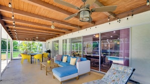A spacious patio area with a wooden ceiling, a ceiling fan, and a pool view. There are yellow chairs, a blue sofa, and a patterned lounge chair. - Heated Saltwater Pool < 2 Mi to Yacht Club Beach! (Cape Coral)