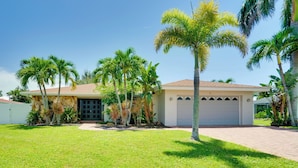 A house with a garage, surrounded by a well-maintained lawn and palm trees. - Heated Saltwater Pool < 2 Mi to Yacht Club Beach! (Cape Coral)
