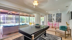 A modern living room with a ping pong table, a sofa, and a dining area with pink chairs. - Heated Saltwater Pool < 2 Mi to Yacht Club Beach! (Cape Coral)
