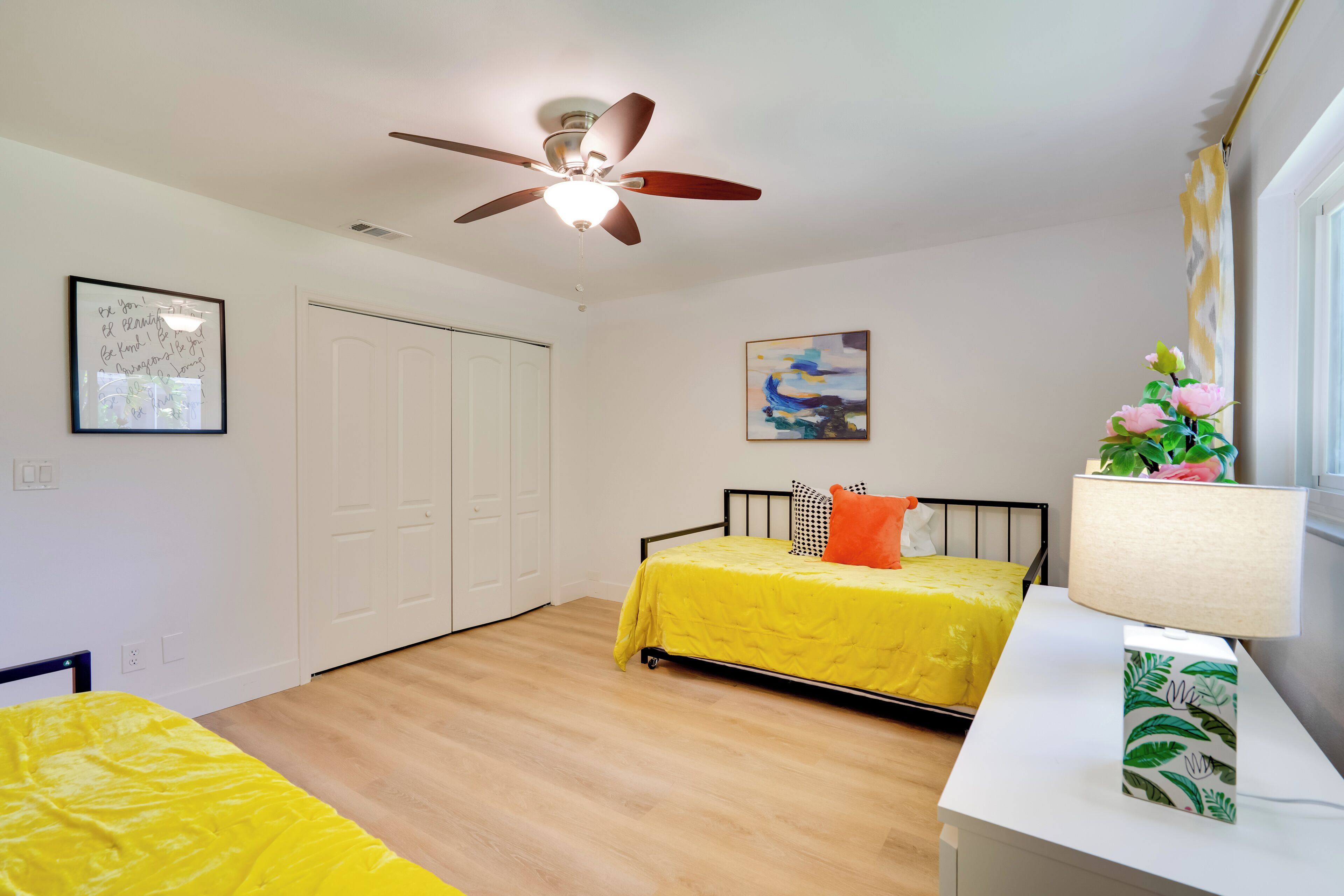 A bedroom with a bed, a desk, a ceiling fan, and a window with curtains.