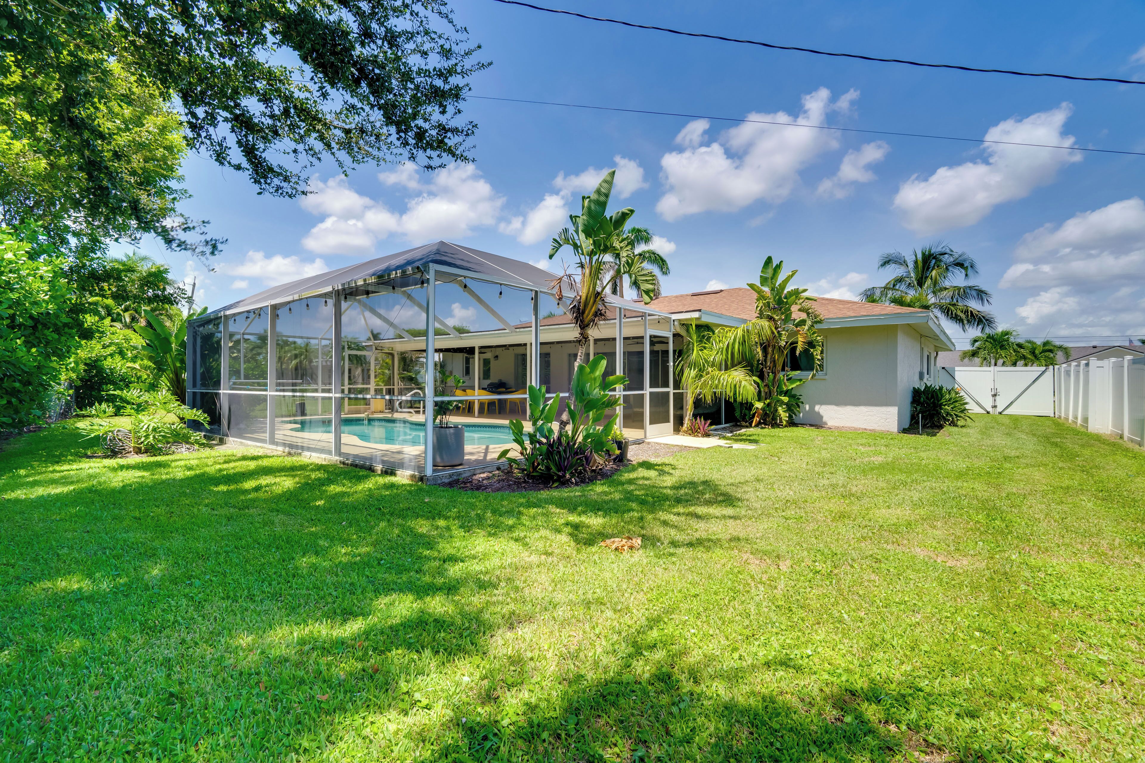A modern house with a glass-enclosed pool, surrounded by lush greenery and palm trees.