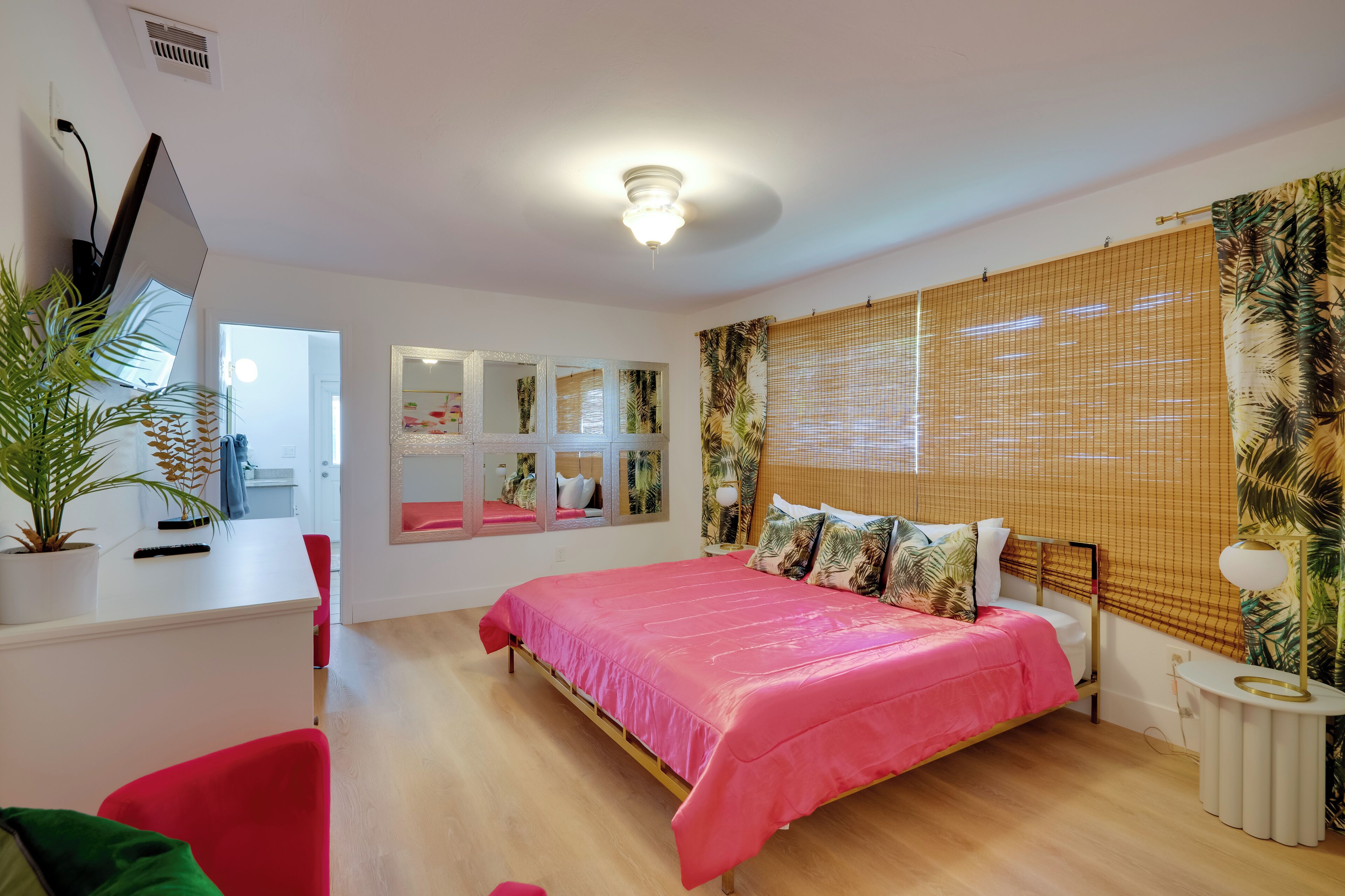 A bedroom with a bed, a desk, a chair, a potted plant, and a window with blinds.