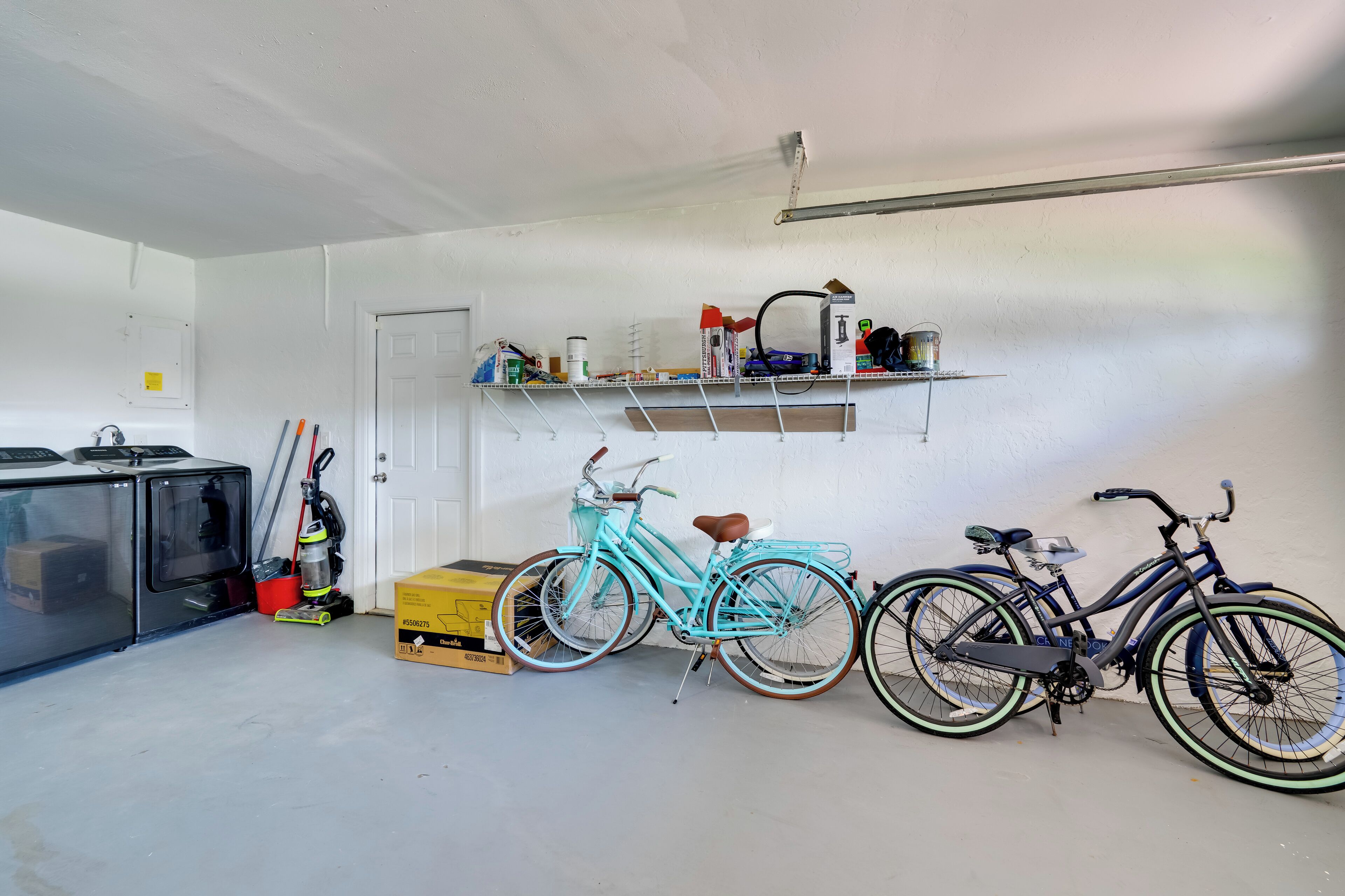 Un garatge amb bicicletes, un aspirador i una estant amb diferents objectes.