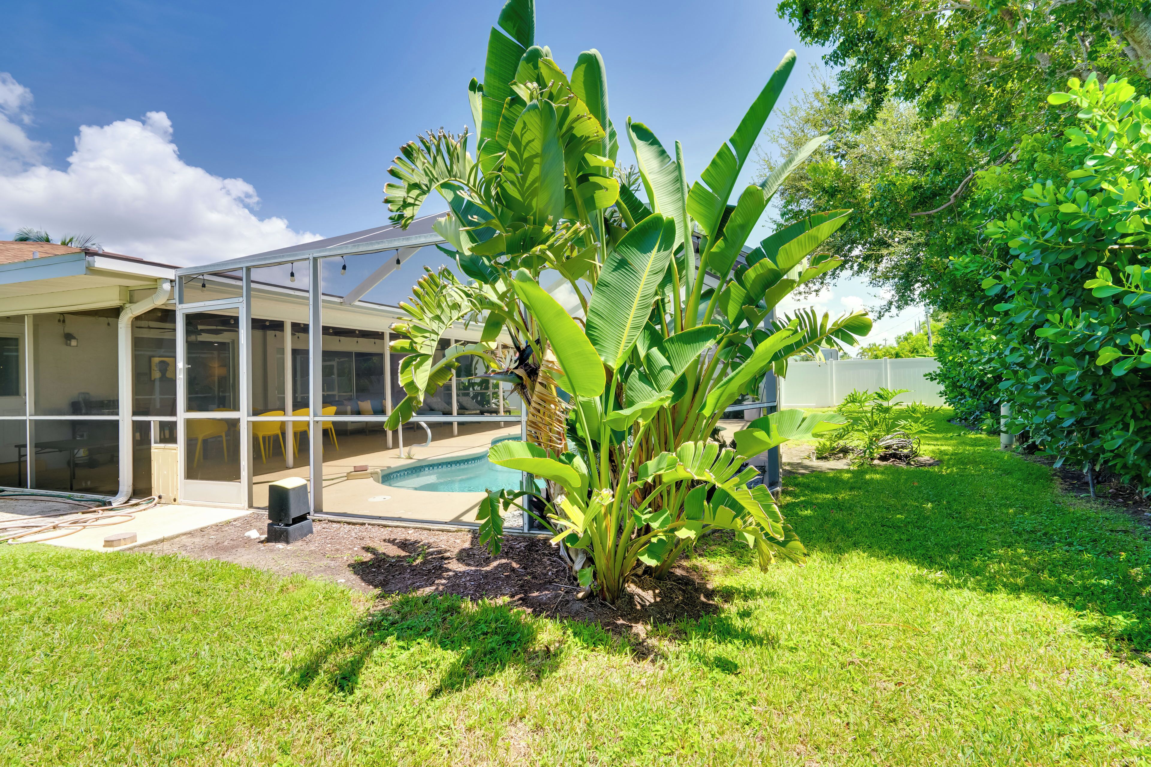 A house with a glass-enclosed patio, a swimming pool, and lush green plants.