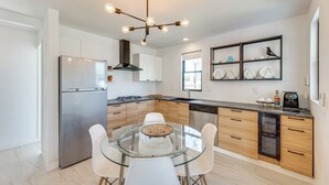 Una cucina moderna con un tavolo da pranzo in vetro, elettrodomestici in acciaio inossidabile, mobili in legno e un lampadario particolare.