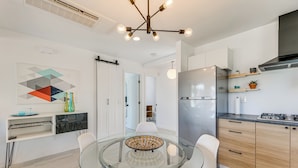 Una cucina moderna con un tavolo da pranzo in vetro, sedie bianche e un frigorifero in acciaio inossidabile.
