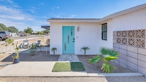 Una casa moderna con una porta turchese, un piccolo patio con sedie e piante di palma.