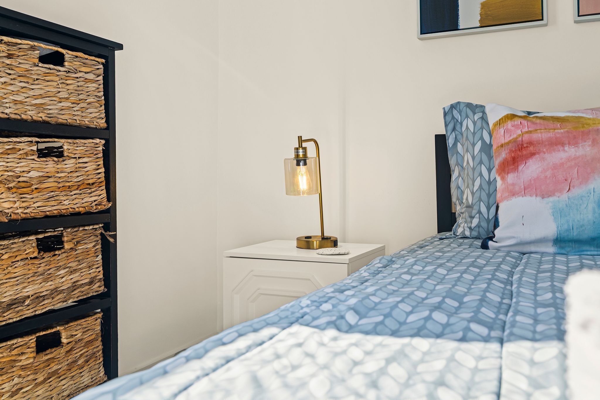 A neatly arranged bedroom with a bed, a bedside lamp, and wicker storage baskets.