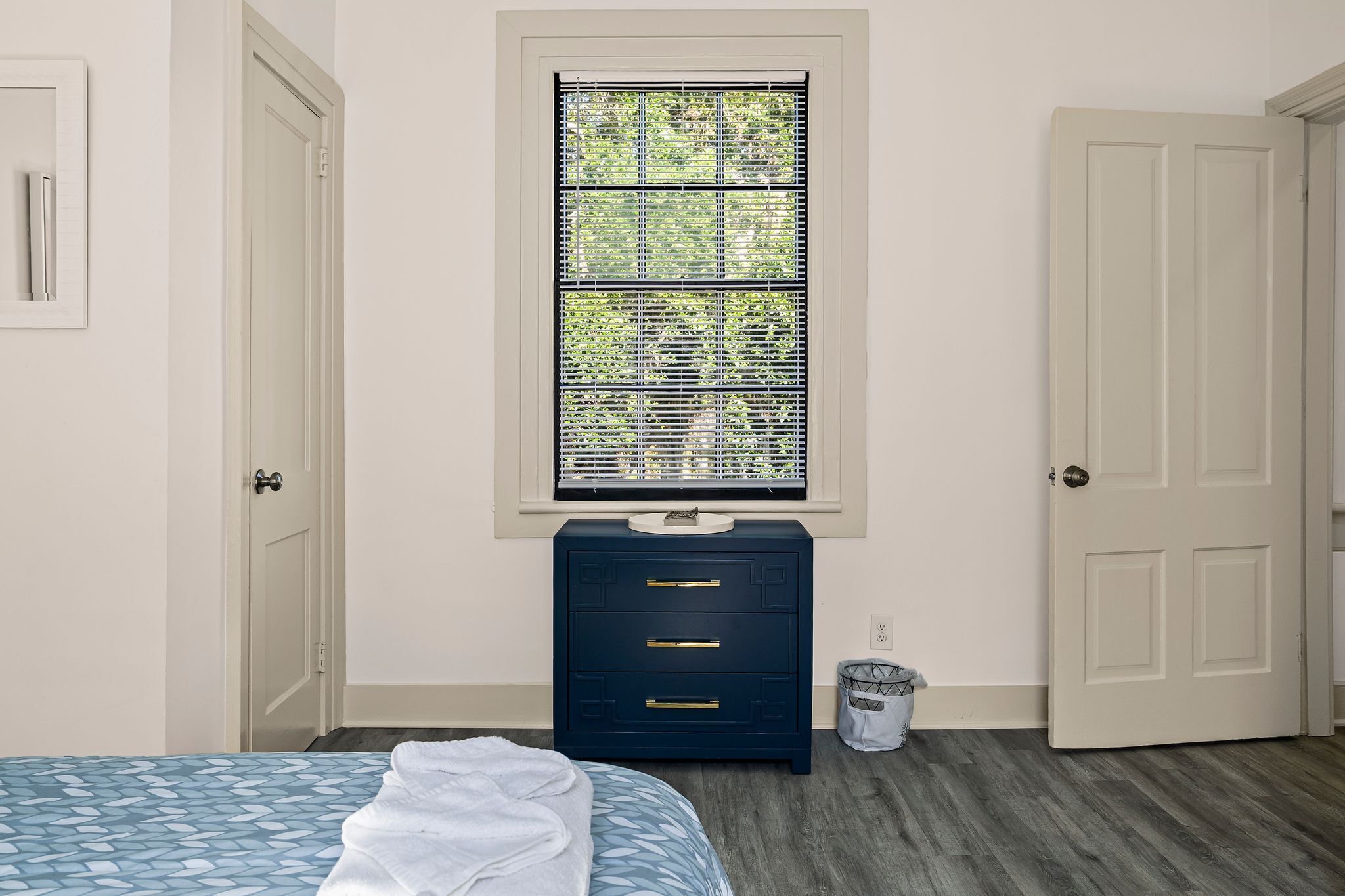 Une chambre à coucher avec un lit, une commode, une fenêtre avec des stores et une porte.
