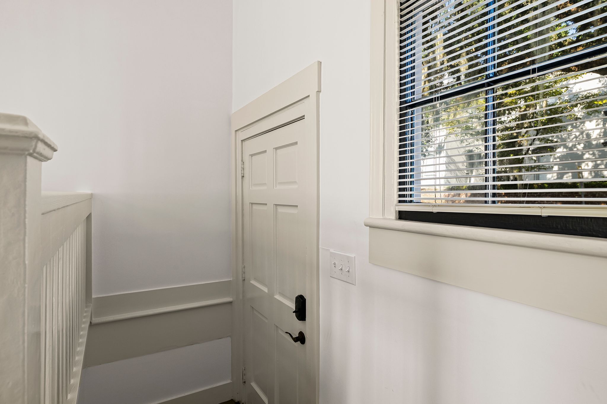 A white door with a black handle, a window with blinds, and a white wall.