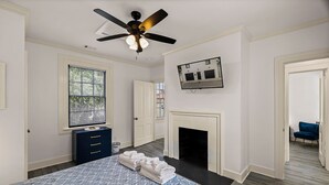 Une chambre à coucher comprenant un lit, un ventilateur de plafond, une cheminée, une fenêtre et un téléviseur fixé au mur.