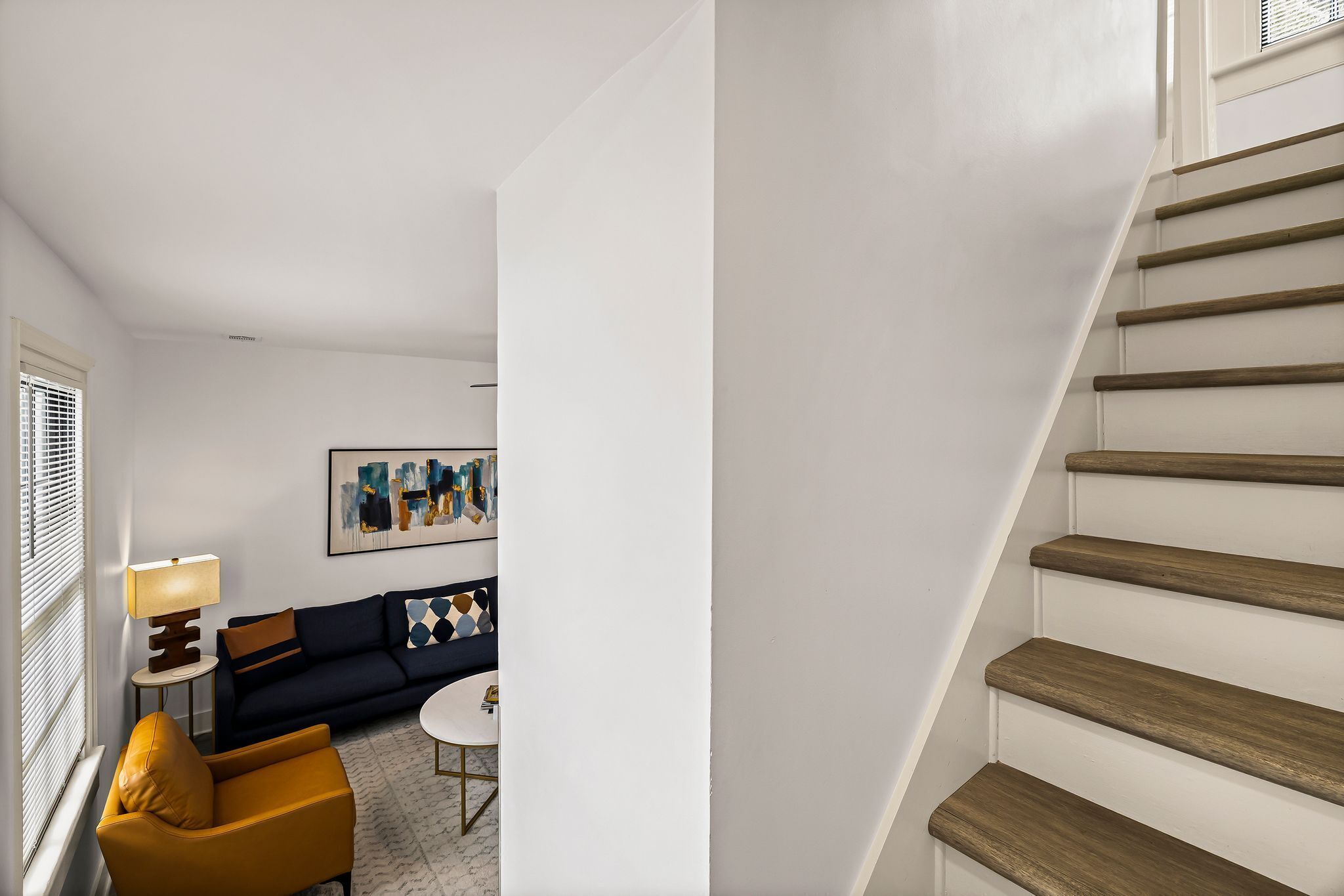 A modern living room with a sofa, armchair, and coffee table, and a staircase with wooden steps.