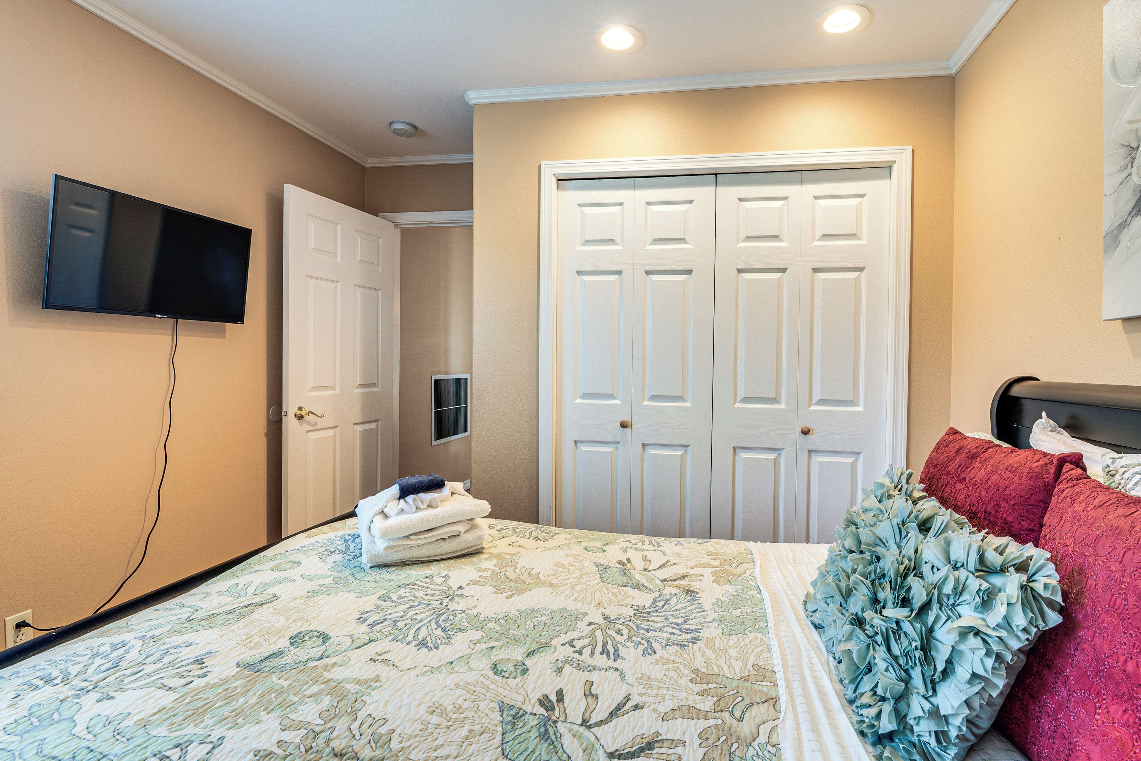 A bedroom with a bed, a television mounted on the wall, and a closet with double doors.